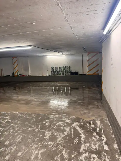 Frisch aufgetragene, noch nasse Beschichtung glänzt auf einem Teil der Tiefgaragenfläche, davor der vorbereitete Untergrund.