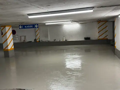 Weite Tiefgaragenfläche mit frisch aufgetragener, glänzender grauer Bodenbeschichtung.