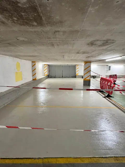 Dieselbe Tiefgaragenrampe nach der Sanierung mit neuer, glatter grauer Bodenbeschichtung und gelben Markierungen.