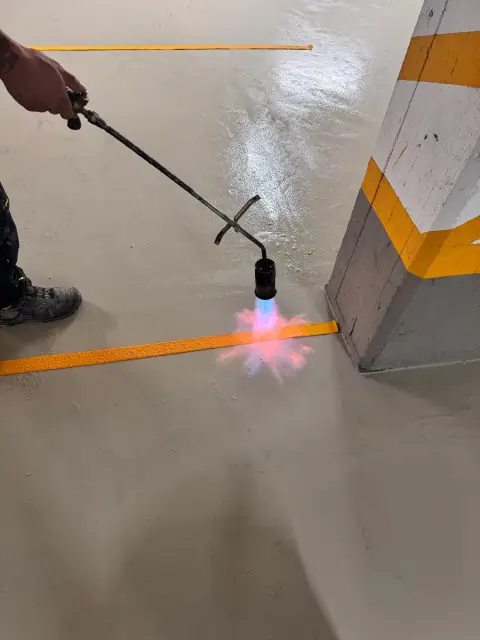 Detail: Eine gelbe Stellplatzmarkierung wird mit dem Gasbrenner auf die neue Bodenbeschichtung aufgebracht.