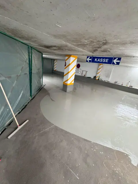 Graue Verlaufsbeschichtung wird in einer Tiefgarage mit dem Rakel über die grundierte Fläche verteilt.
