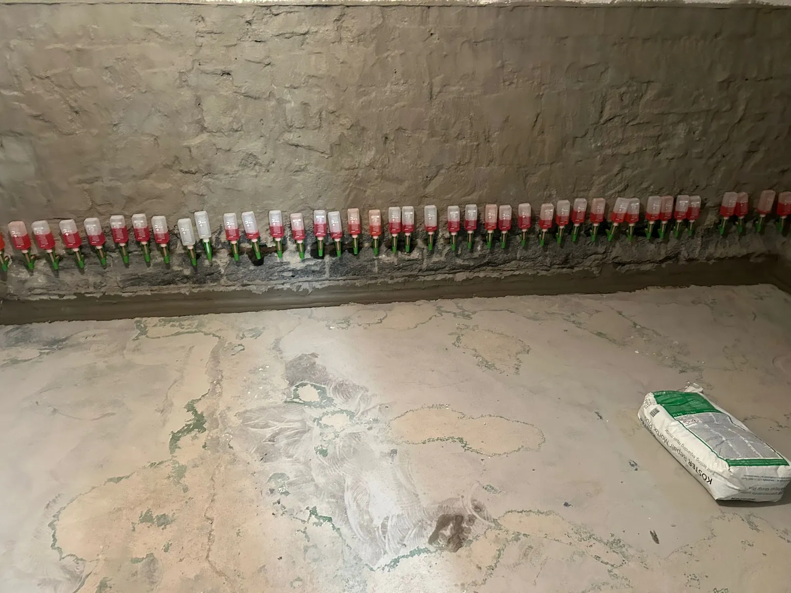 Kellerwand mit einer Reihe von Injektionskartuschen am Wandfuß: Eine Horizontalsperre gegen aufsteigende Feuchtigkeit wird eingebracht.