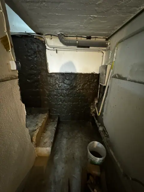 Kellerabgang mit frisch aufgetragener dunkler Abdichtungsschicht an Wänden und Boden als Innenabdichtung.