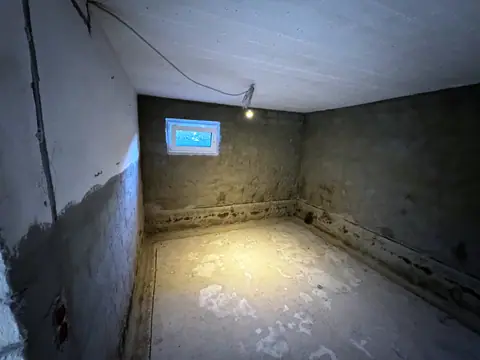 Kellerraum mit entferntem Putz und feuchtem Wandfuß, eine Baulampe hängt an der Decke.