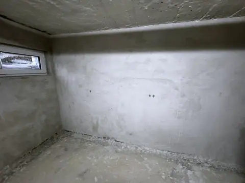 Kellerraum mit frischem Sanierputz an allen Wänden und einem kleinen Kellerfenster, der Boden noch staubig.