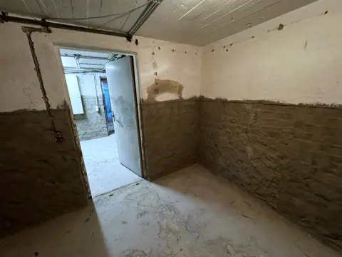 Kellerraum mit abgeschlagenem Putz im unteren Wandbereich, Blick durch die offene Tür in den Nebenraum.