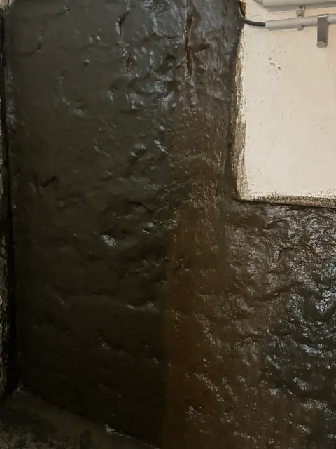 Nahaufnahme der schwarzen Abdichtungsschicht auf einer Kellerwand, flächig und lückenlos aufgetragen.