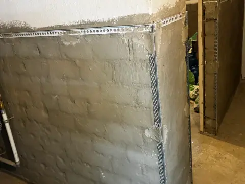 Detail einer Kellerwand mit Sanierputz-Grundschicht, Putzabschlussprofil oben und Eckschutzschiene an der Kante.