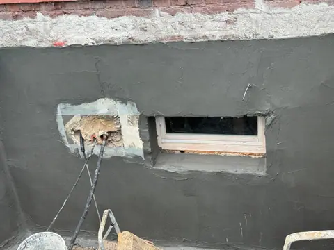 Kellerfenster von außen, das Mauerwerk rundum ist mit frischer dunkler Abdichtung versehen.