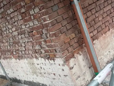 Klinkerfassade mit neu abgedichtetem dunklem Sockel hinter einem Gerüst.