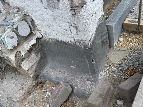 Fuß eines Mauerpfeilers mit frischer dunkler Abdichtung über dem Kiesbett.