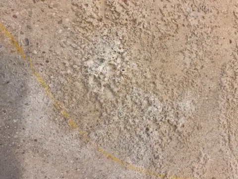 Nahaufnahme eines Risses im Betonboden einer Halle, die Oberfläche ist rau und fleckig.
