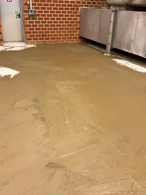 Ausgleichsmasse in einer Industriehalle frisch aufgezogen: Sie gleicht Unebenheiten im Boden vor der Beschichtung aus.