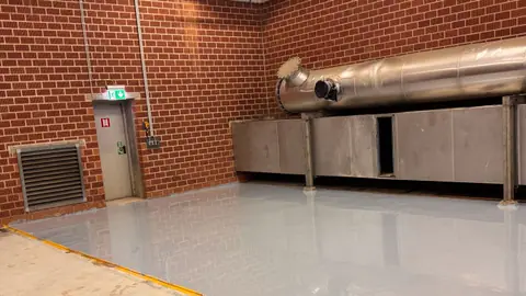 Fertig beschichteter hellgrauer Hallenboden vor einer Klinkerwand, die Fläche glänzt gleichmäßig.