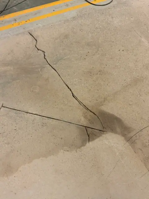 Gerissener Betonboden in einer Industriehalle: mehrere Risse ziehen sich durch die Fläche, daneben Ölflecken.