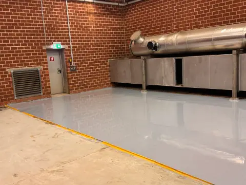 Fertige hellgraue Bodenbeschichtung in einer Industriehalle mit Klinkerwänden, glatt und glänzend.