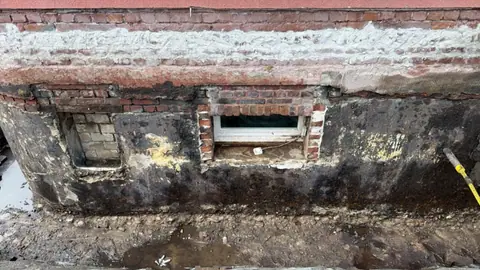 Freigelegtes Kellerfenster von außen, das Mauerwerk darum ist feucht und verschmutzt, vor der Abdichtung.