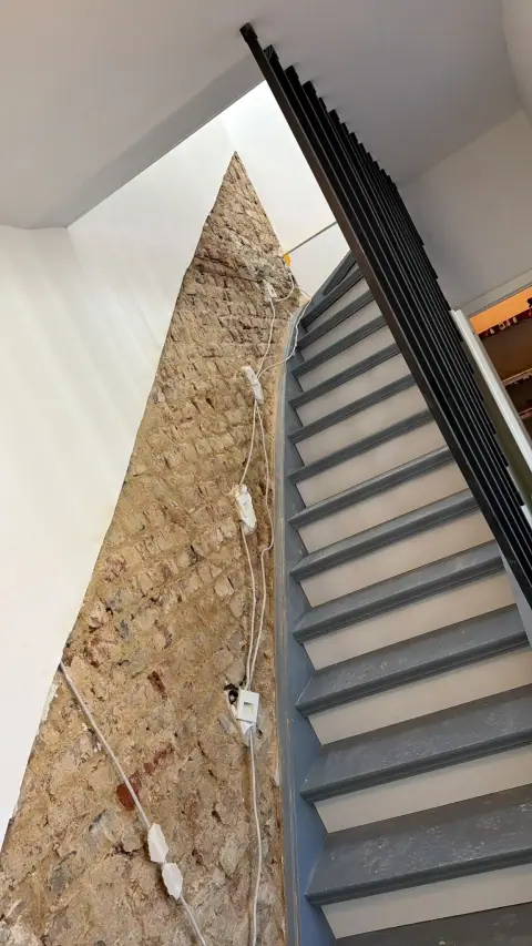 Treppenhauswand vor der Sanierung: Der Putz ist entfernt, das feuchte Ziegelmauerwerk liegt frei.