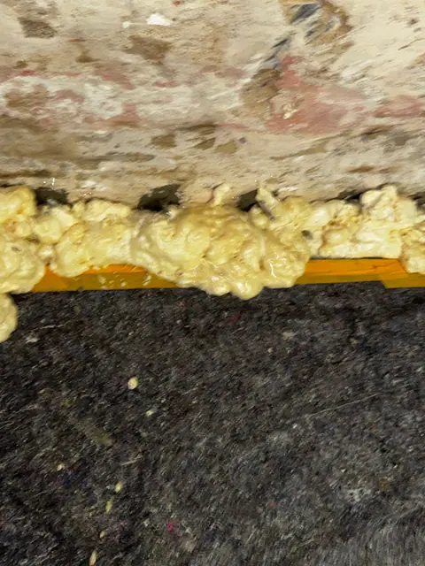 Ausgehärteter Injektionsschaum quillt am Wandfuß aus der abgedichteten Fuge.