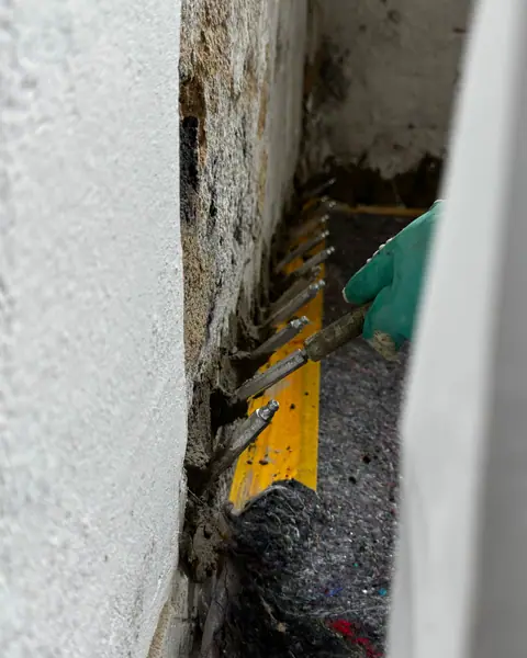 Reihe von Stahlpackern in einer Wand am Boden, eine Hand mit Schutzhandschuh setzt den nächsten.
